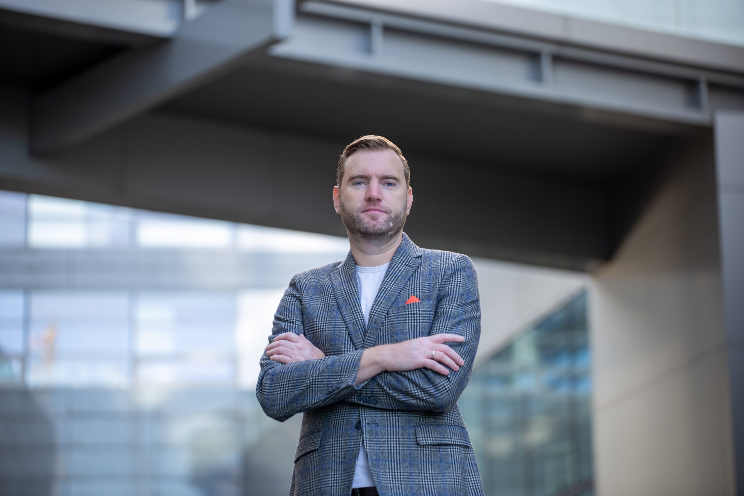Man in gray blazer stands confidently with arms crossed.