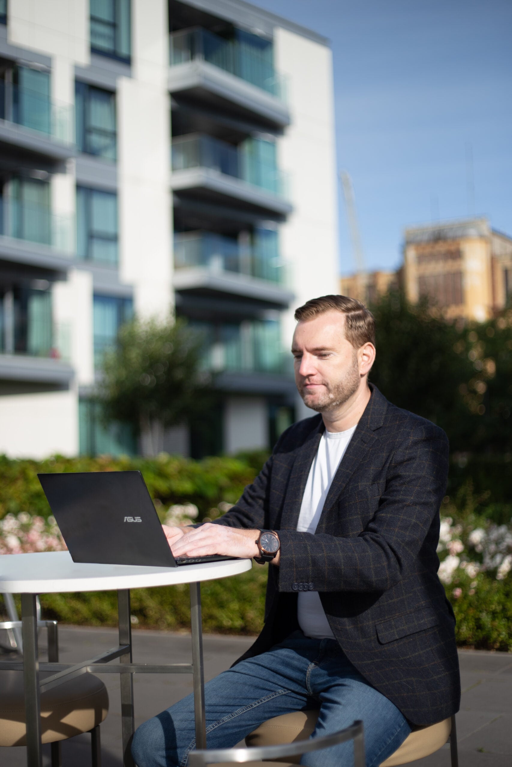 Man typing on laptop outdoors near building.